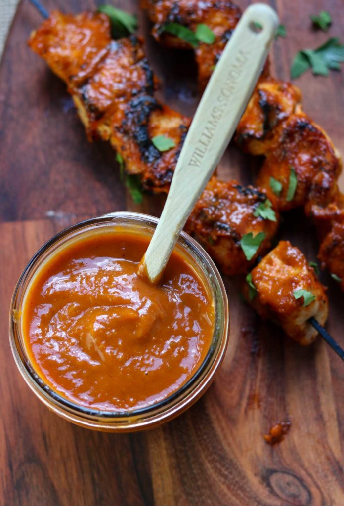 Mango Jalapeno BBQ Sauce in a mason jar with a bbq brush, grilled chicken skewers in the background 