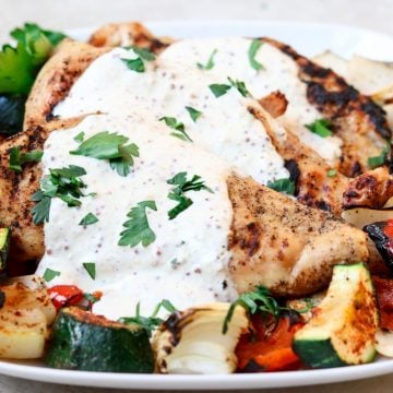 grilled chicken topped with cream sauce and grilled veggies