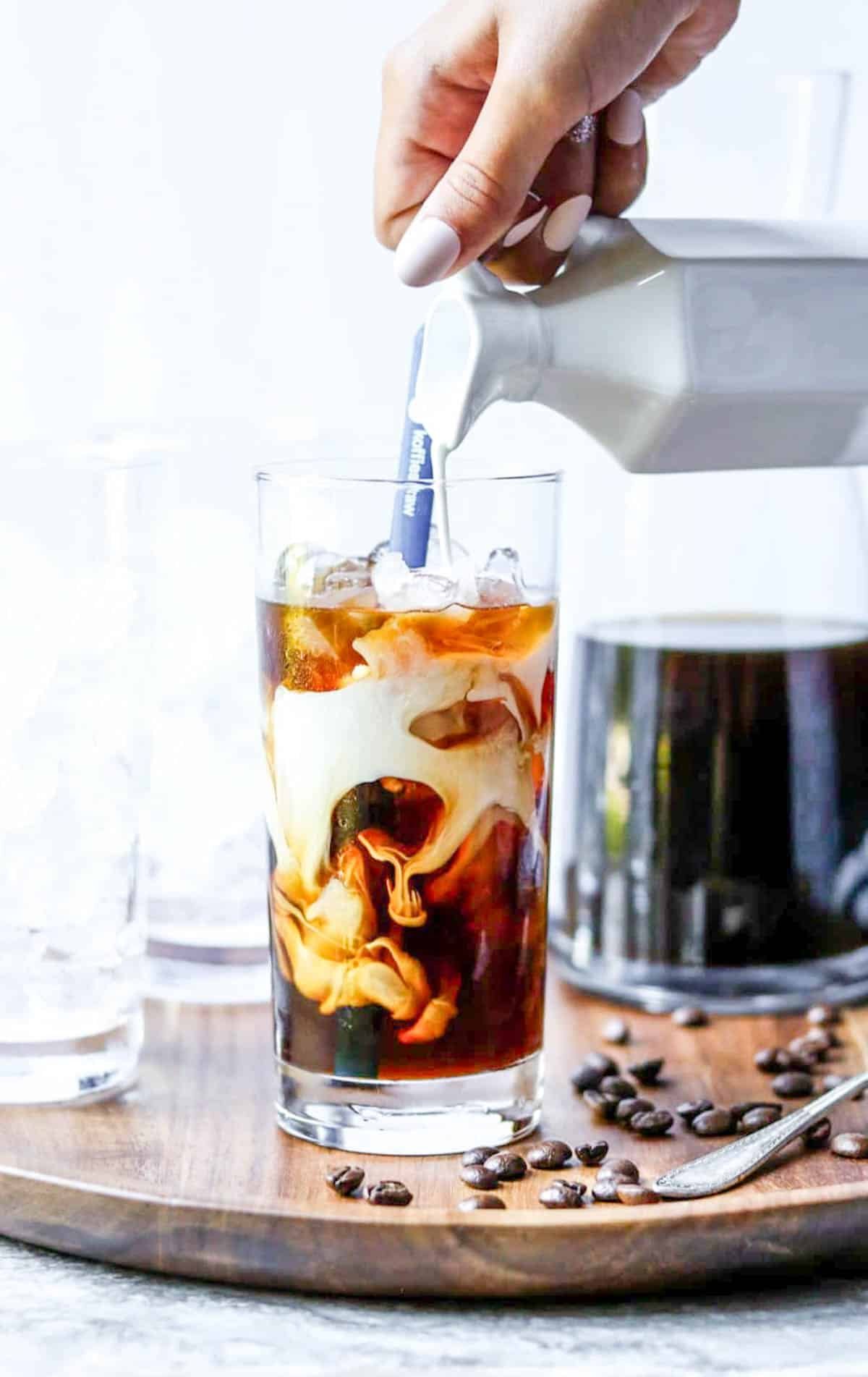 Pouring milk into a glass of cold brew coffee making an iced latte