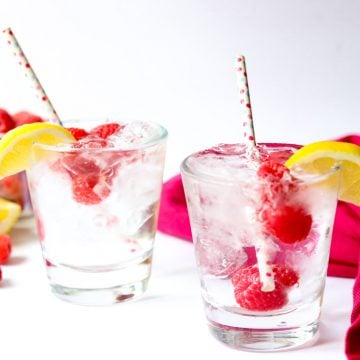 two raspberry vodka sodas garnished with raspberries and lemons