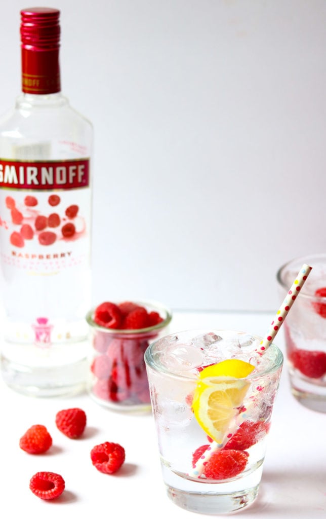 a cocktail with a bottle of vodka and fresh raspberries in the background