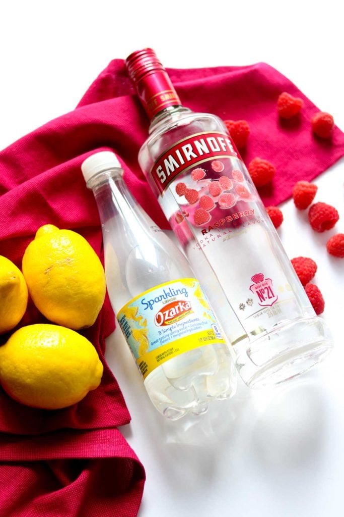 a bottle of raspberry vodka, lemon soda water, and lemons and raspberries