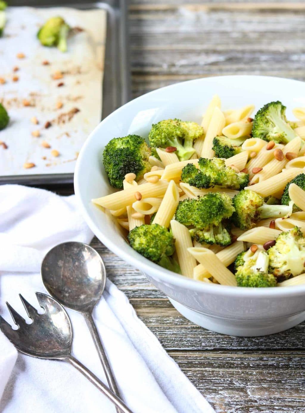 Serving bowl full of pasta and broccoli, serving utensils to the side