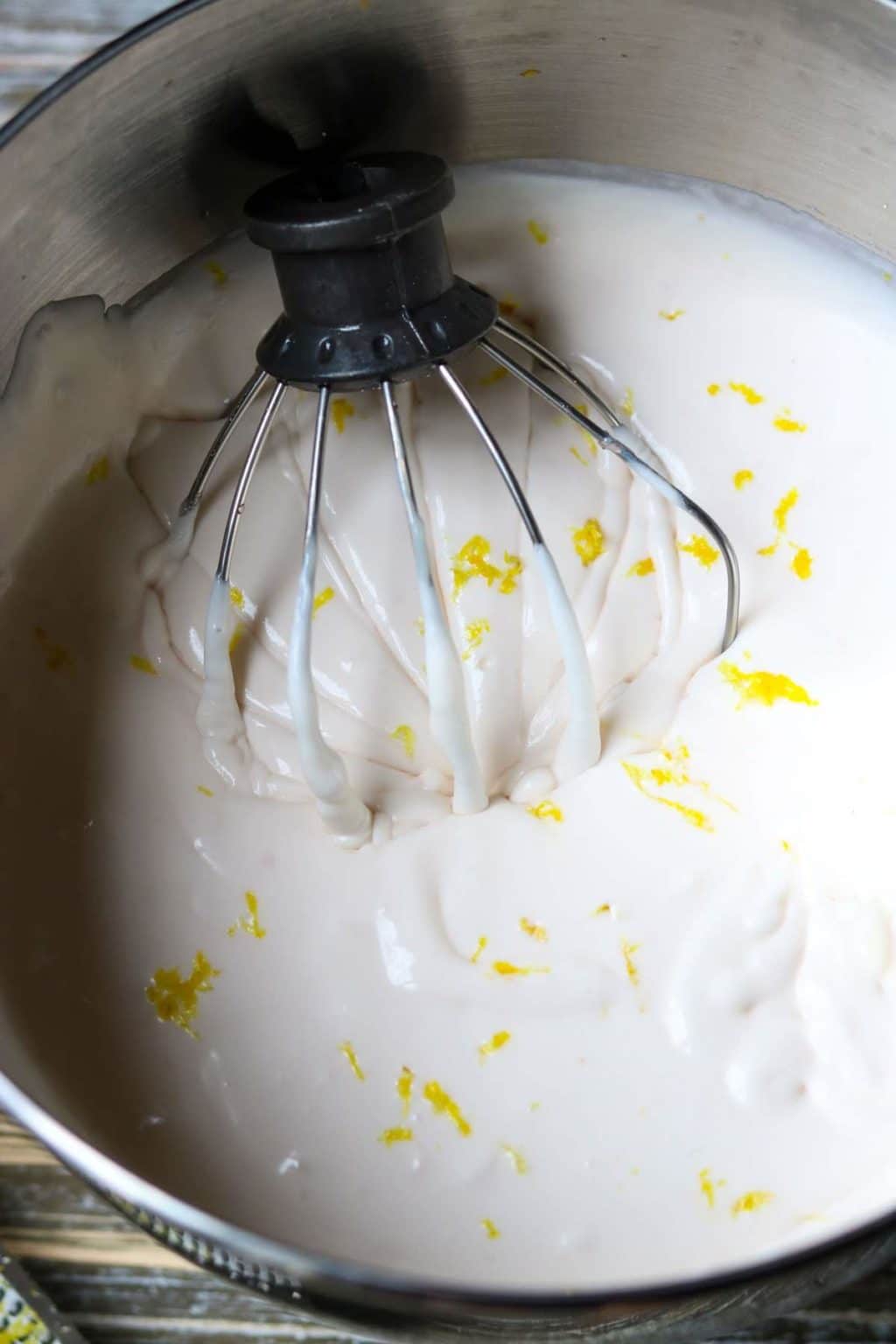 Light pink filling dotted with lemon zest in a kitchen aid stand mixer bowl with the whisk attachment