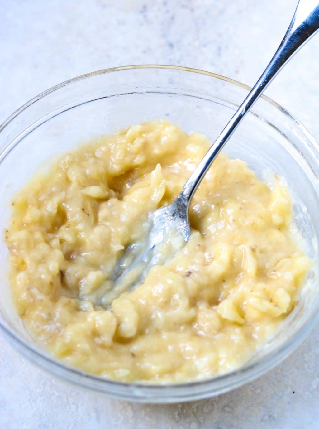 Over-ripe bananas mashed in a bowl with a fork