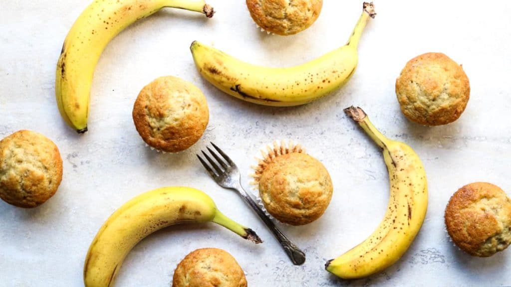 Over-ripe bananas scattered around baked banana bread muffins sitting on a counter
