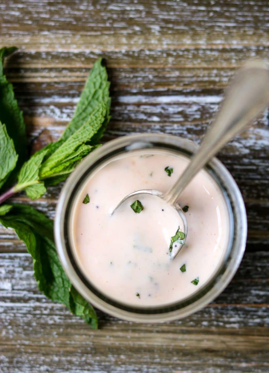 over head picture of raspberry mint aioli in a jar with a spoon with a mint leaf to the side