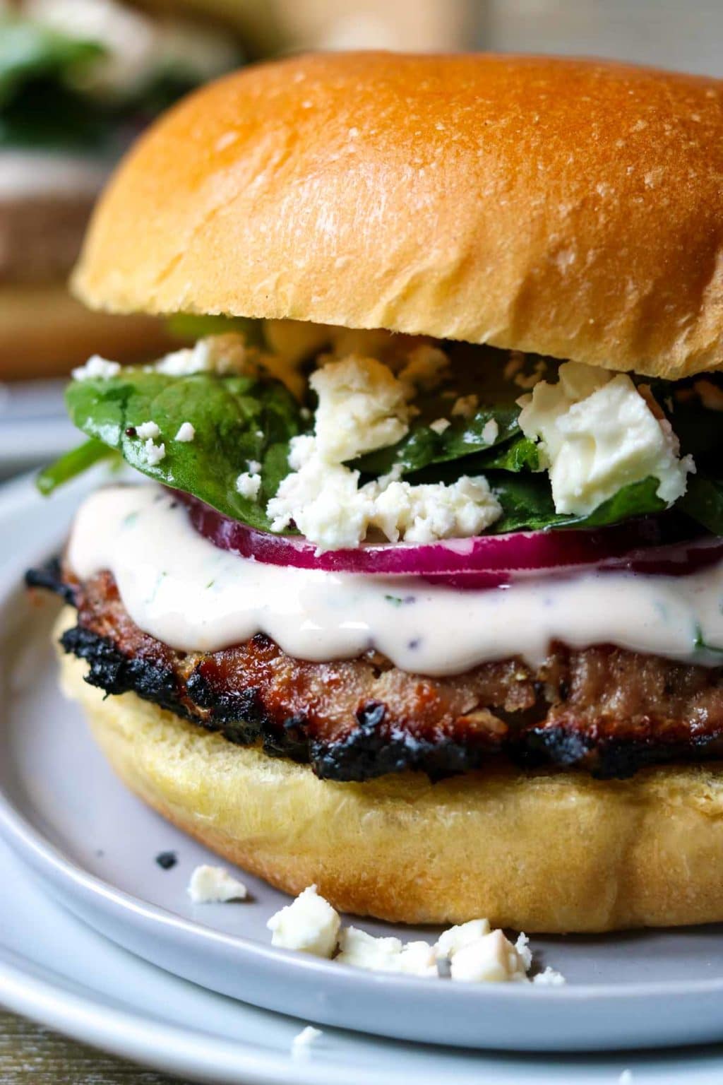 up close picture of the Greek Turkey Burger with Raspberry Mint Aioli, feta cheese spilling over the edge, on a small grey plate