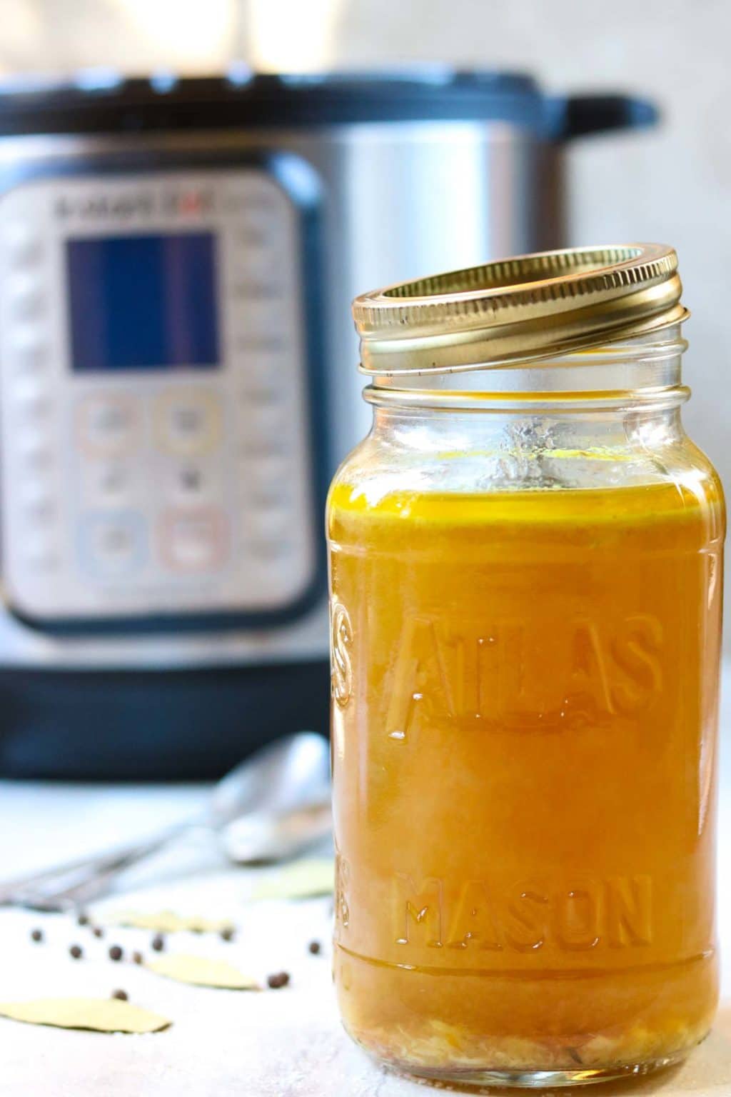 A mason jar full of Instant Pot Chicken Broth with an Instant Pot in the background