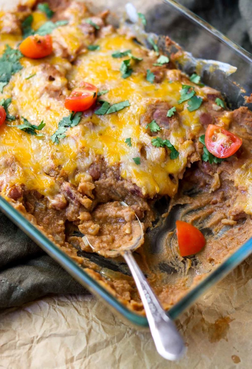 A baking dish of refried beans topped with cheese, cilantro and tomatoes