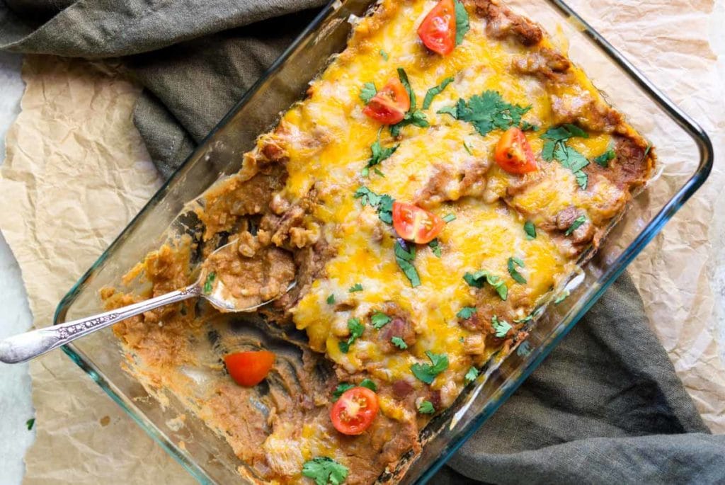a baking dish full of refried beans topped with cheese, cilantro and tomatoes