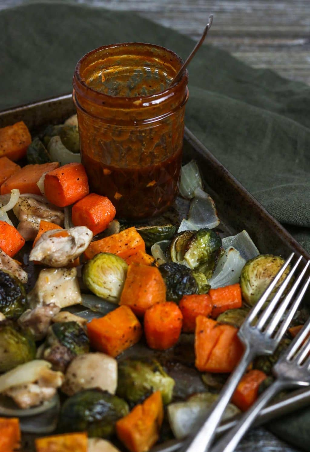 Sheet pan of roasted veggies and chicken with a mason jar of BBQ vinaigrette and two forks