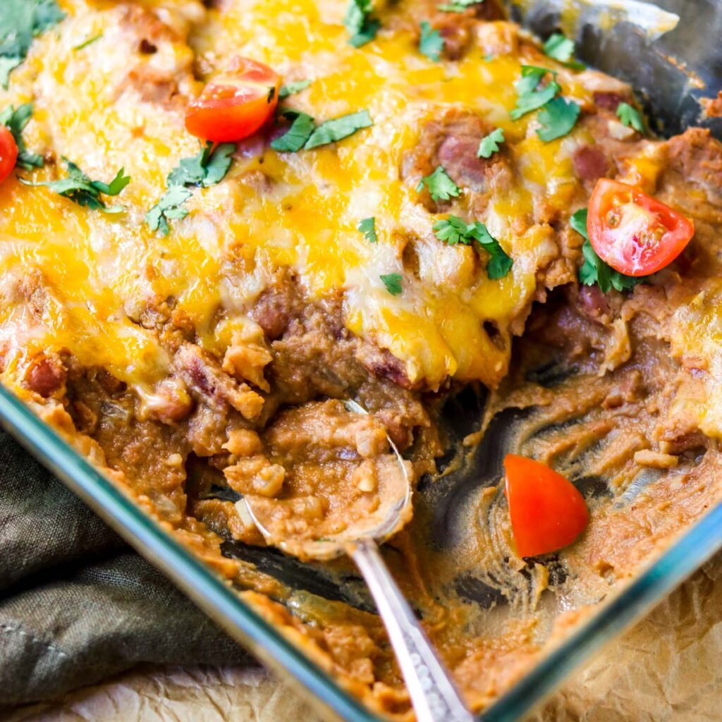 a pan of refried beans topped with cheese, cilantro and tomatoes