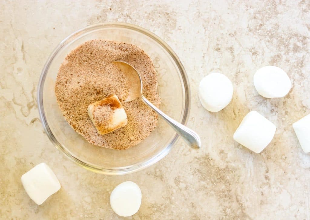 Buttered marshmallows being rolled in a cinnamon sugar mixture