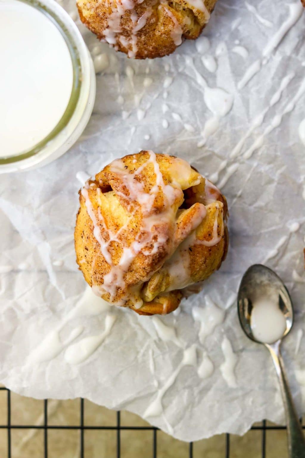 One Cinnamon Bun drizzled with Powder Sugar Glaze and a spoon full of glaze to the side