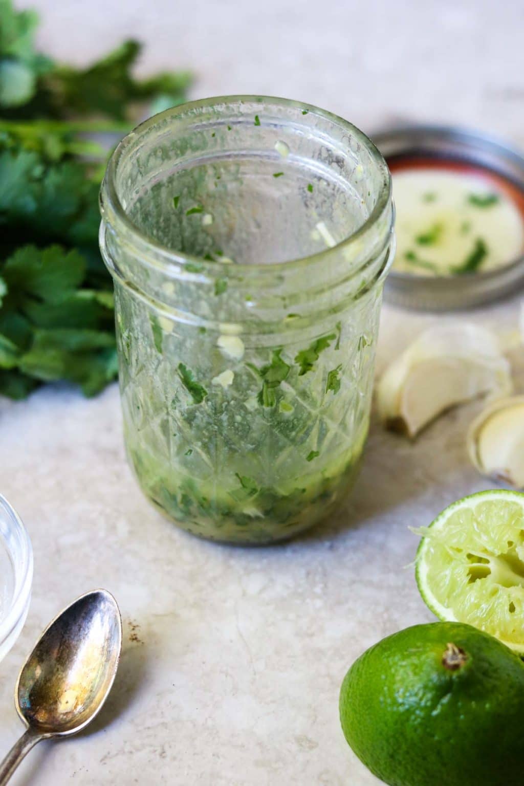 Cilantro Lime Vinaigrette in a mason jar with cilantro, garlic, and squeezed limes on the counter