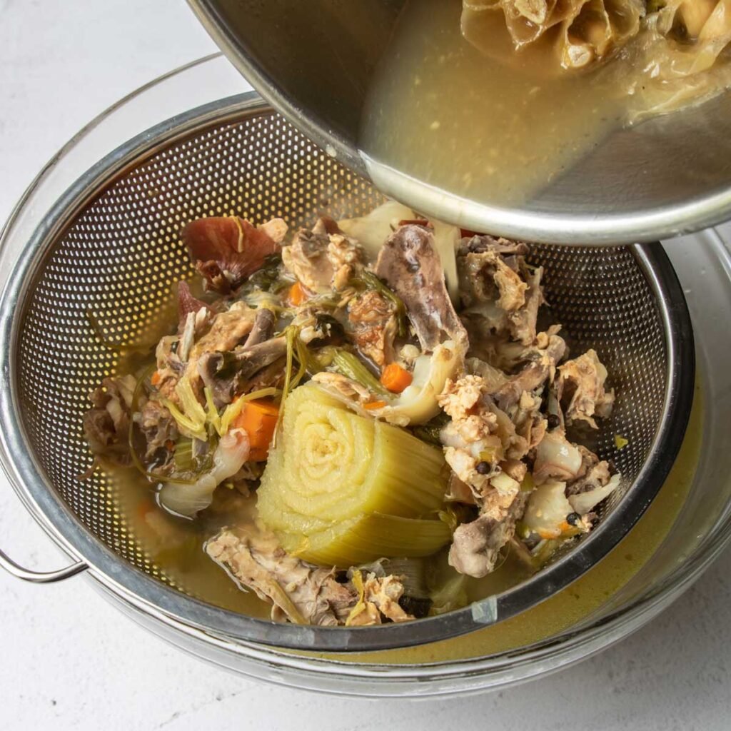 straining the solids from chicken stock