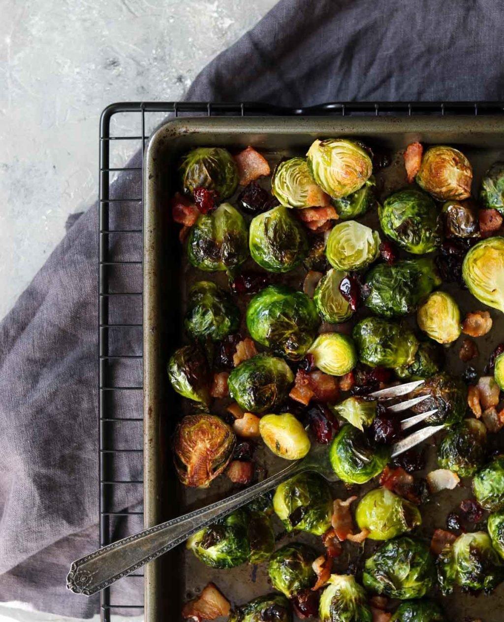 Oven roasted brussels sprouts on a sheet pan with a fork sitting on a black cooling rack