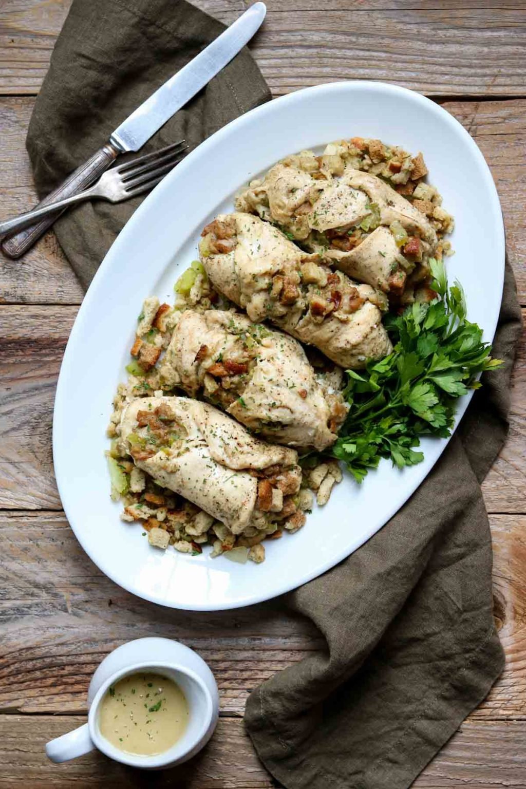 Chicken with Stuffing on a white oval serving platter garnished with parsley, a knife and fork and gravy to the side