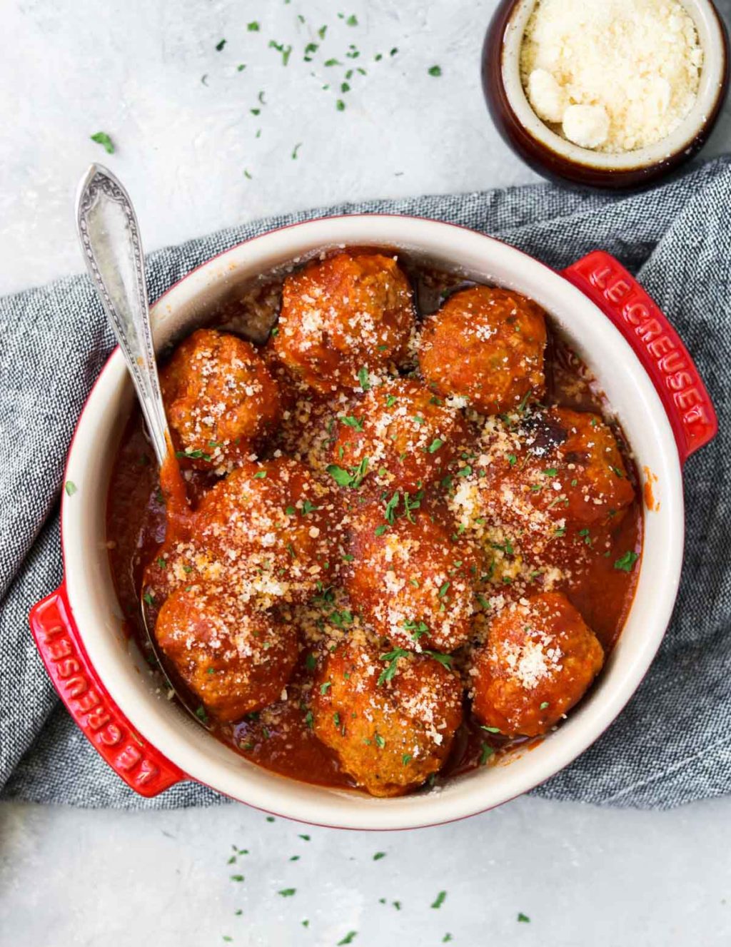 Turkey meatballs in a red dish garnished with parmesan cheese and parsley