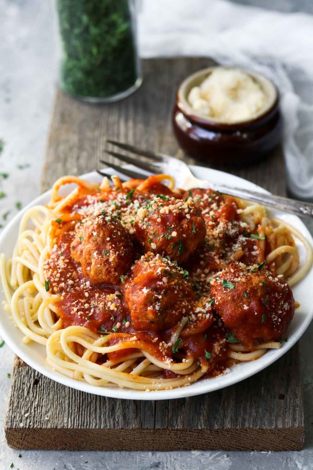 Turkey meatballs over spaghetti on a white plate on a wood board