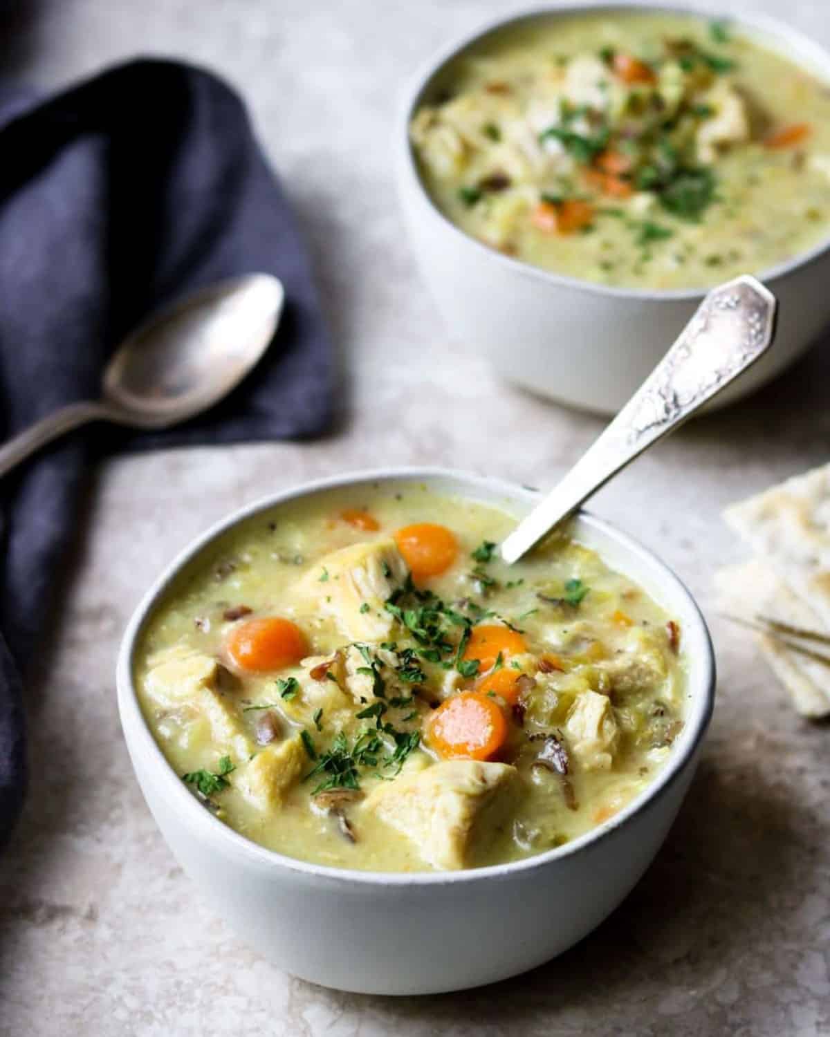 two bowls of chicken and rice soup with spoons and crackers