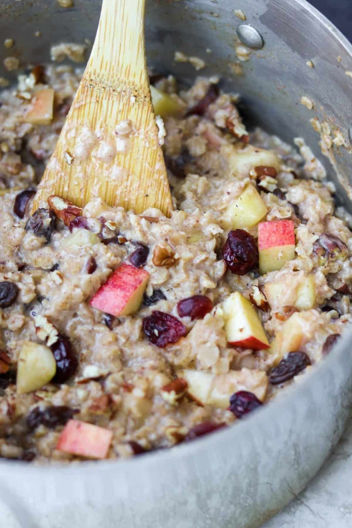 a pot full of cooked oatmeal with cranberries, apples and nuts