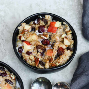 a black bowl filled with oatmeal with fruit, milk and nuts
