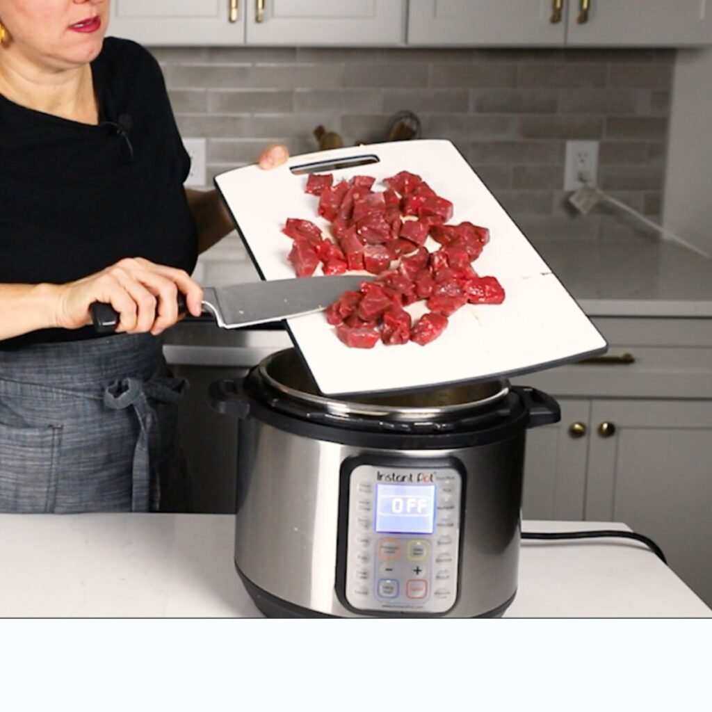 Susie Scraping beef stew meat off a cutting board into the Instant Pot
