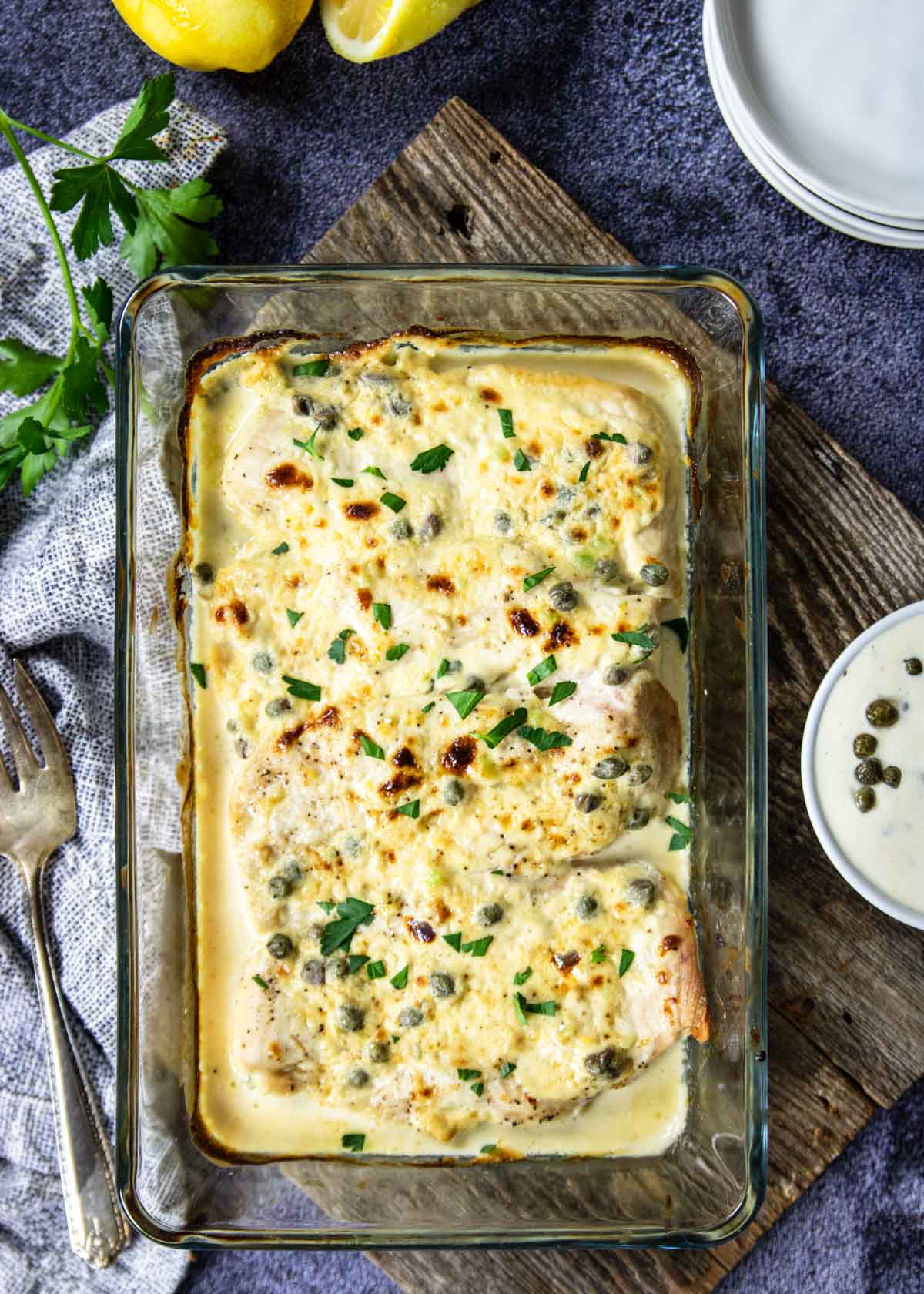 glass baking dish with chicken topped with cream sauce with capers