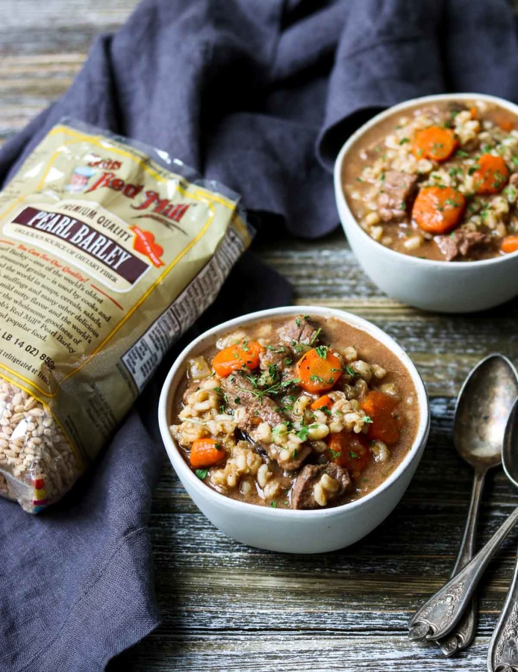 two bowls of beef and barley soup with a bag of bobs red mill pearl barley to the side