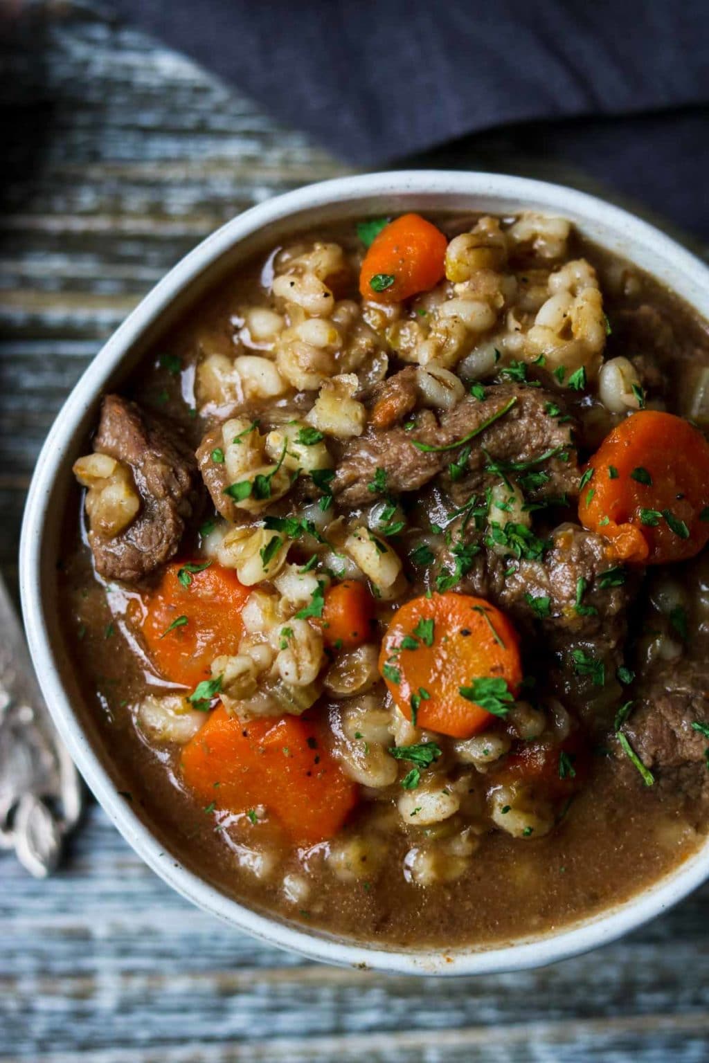 a white bowl full of beef and barley stew on a wooden counter