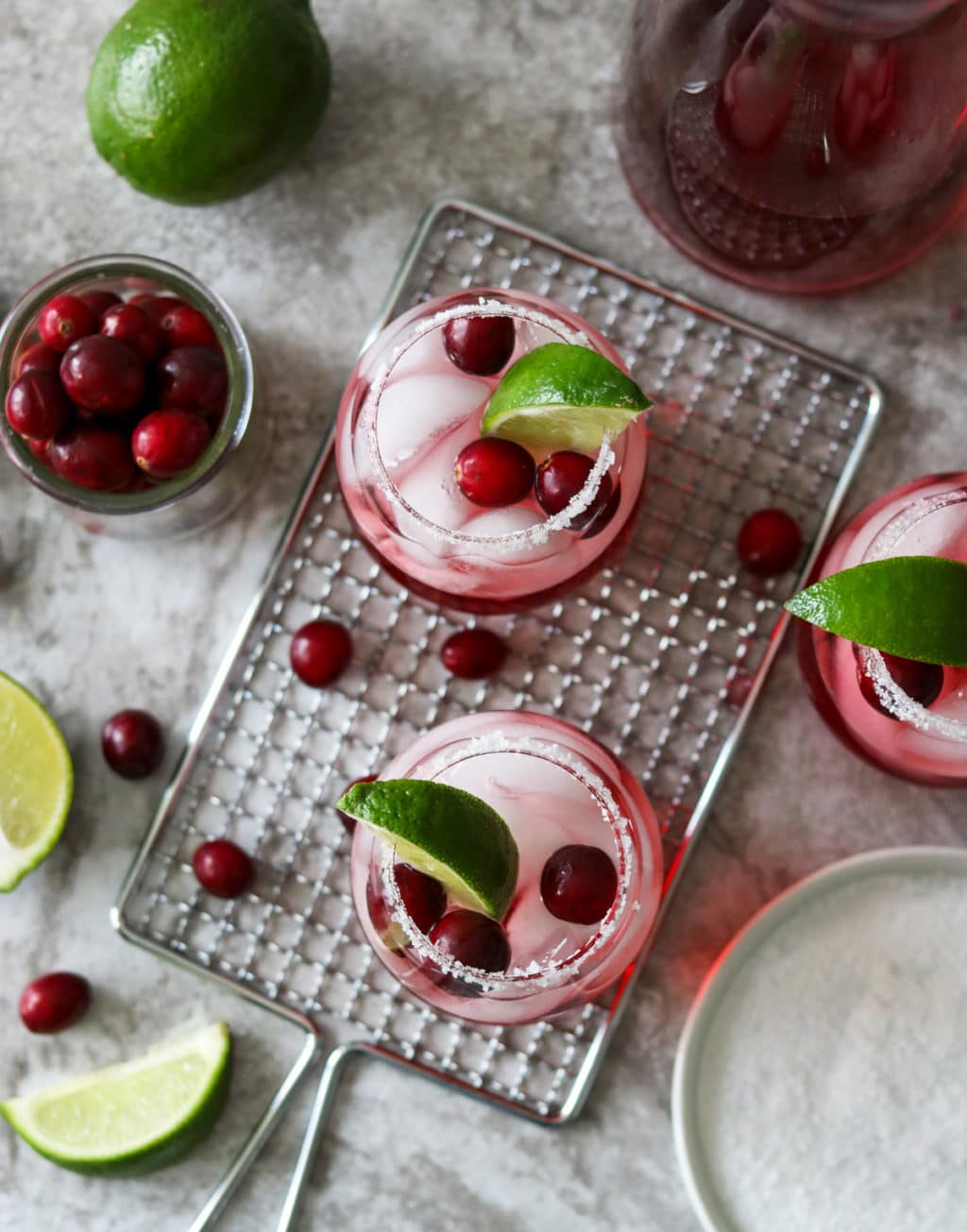 three cranberry ginger margaritas with limes and cranberries scattered on the counter