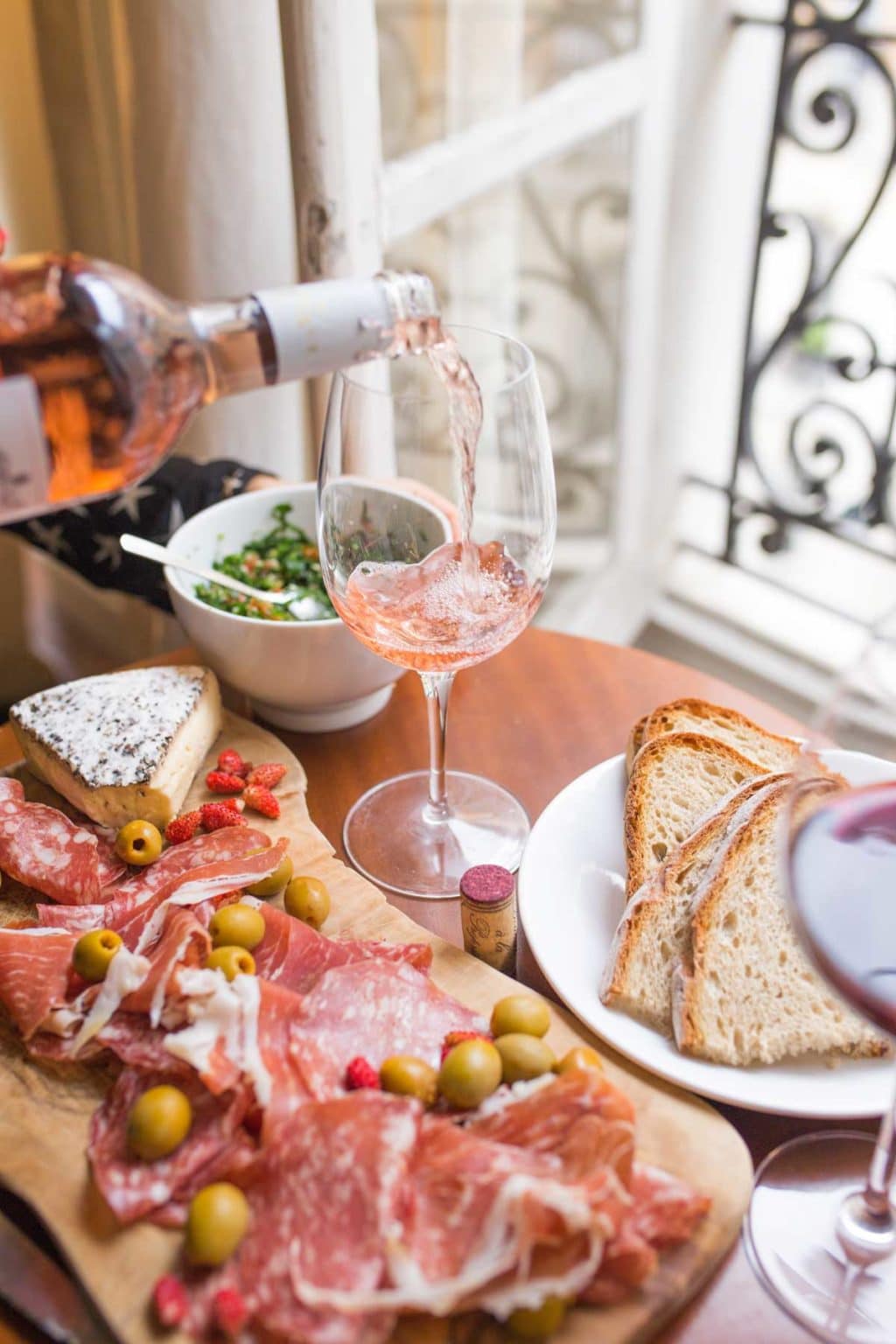 meat and cheese tray with rose wine being poured in a glass