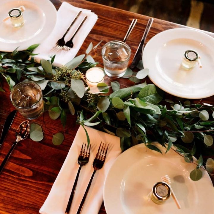 a table with white place settings and green garland