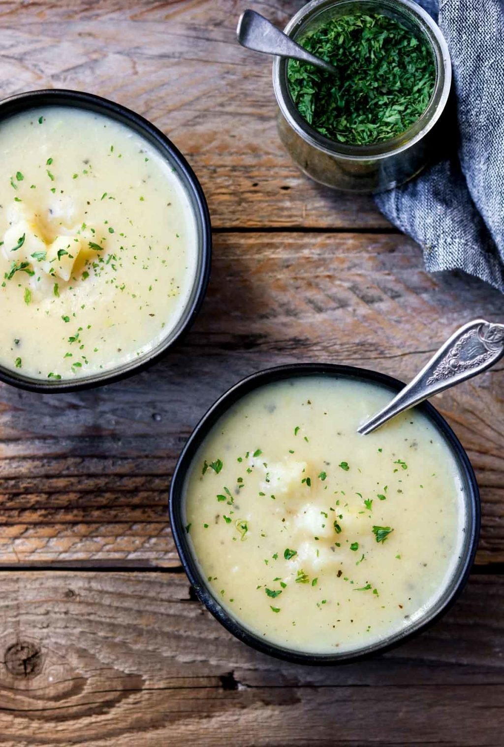 Two black bowls of instant pot creamy potato soup and a glass jar of parsley