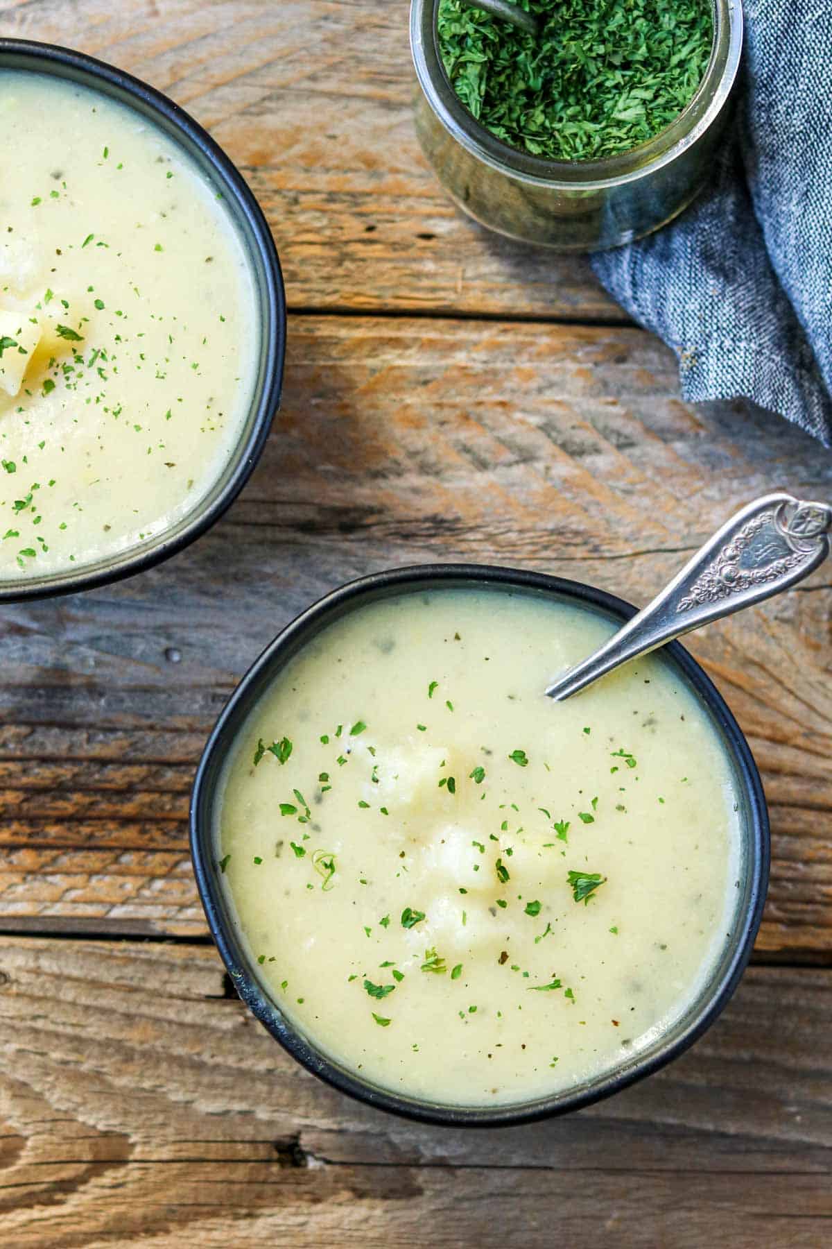two bowls of potato soup with a bowl of parsley to the side