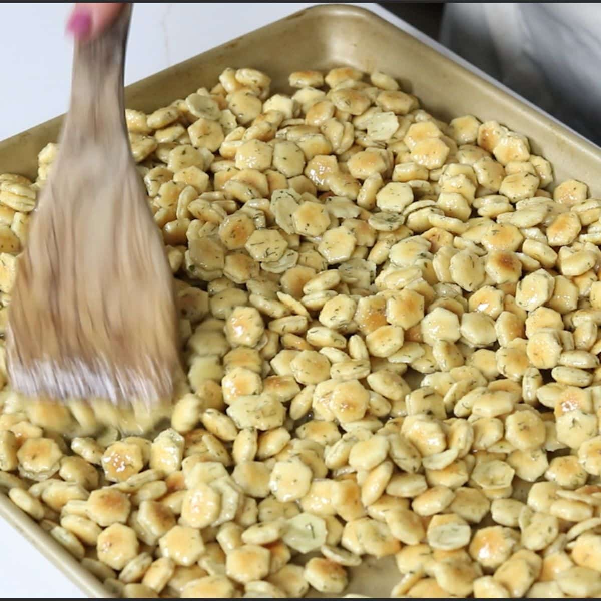 spreading seasoned oyster crackers on a baking sheet for the oven