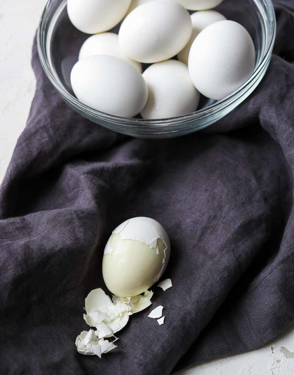 A bowl of hard boiled eggs cooked in the instant pot and one egg half peeled