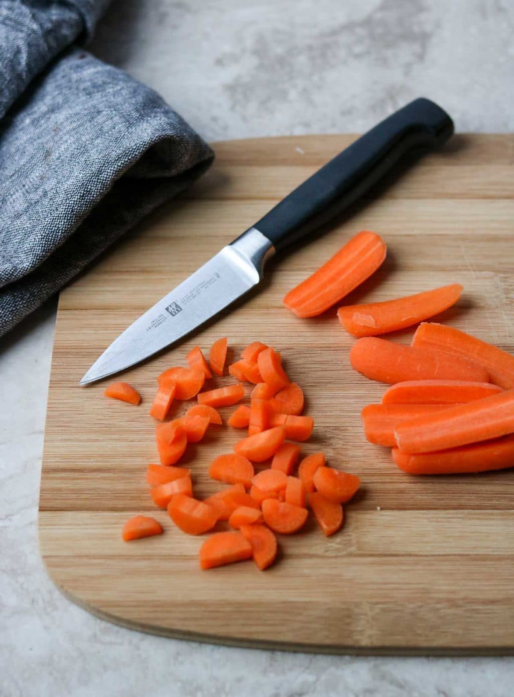 Baby Carrots cut into a small dice on a cutting board with a knife for kids chicken noodle soup