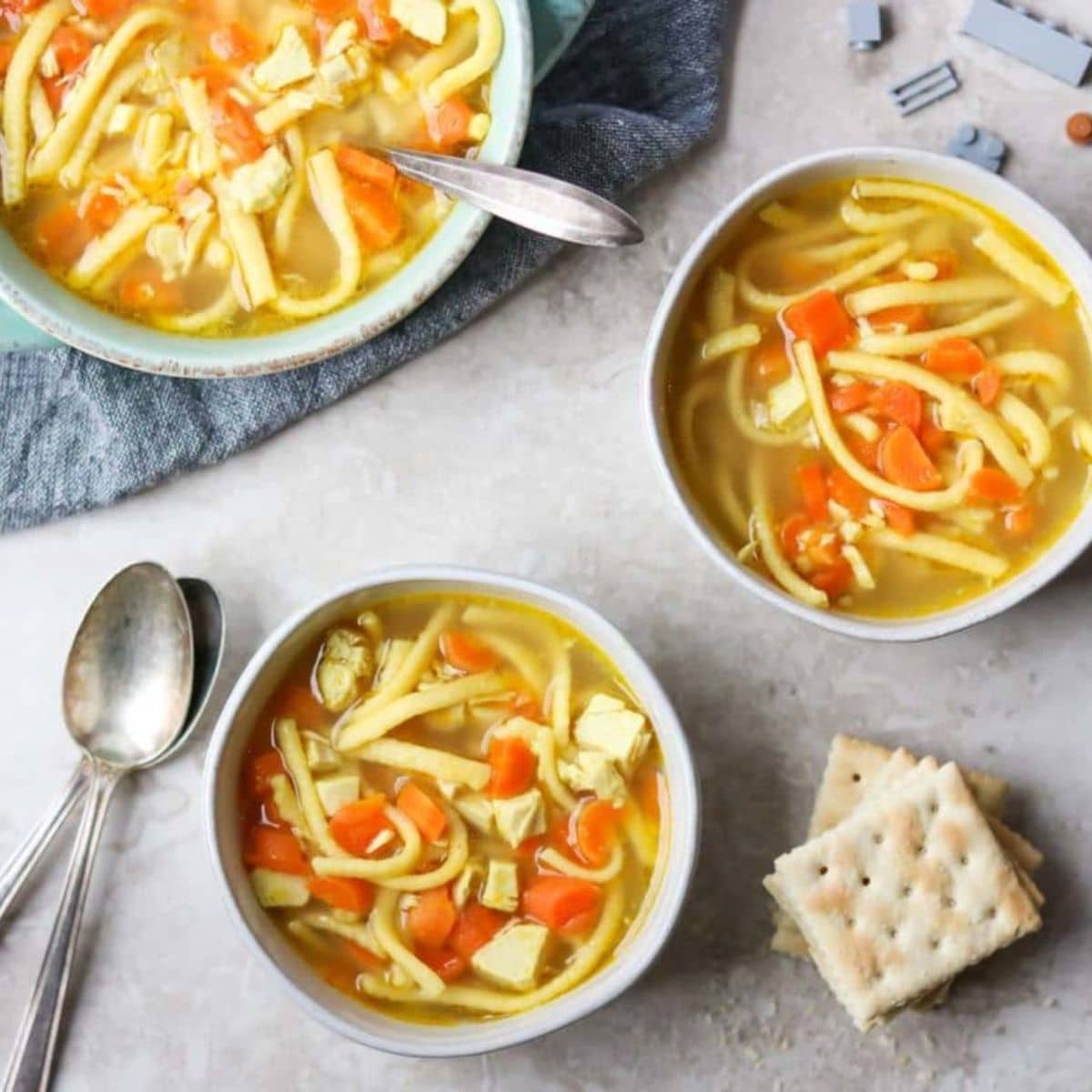 two bowls of chicken noodle soup for kids with legos and crackers around the table