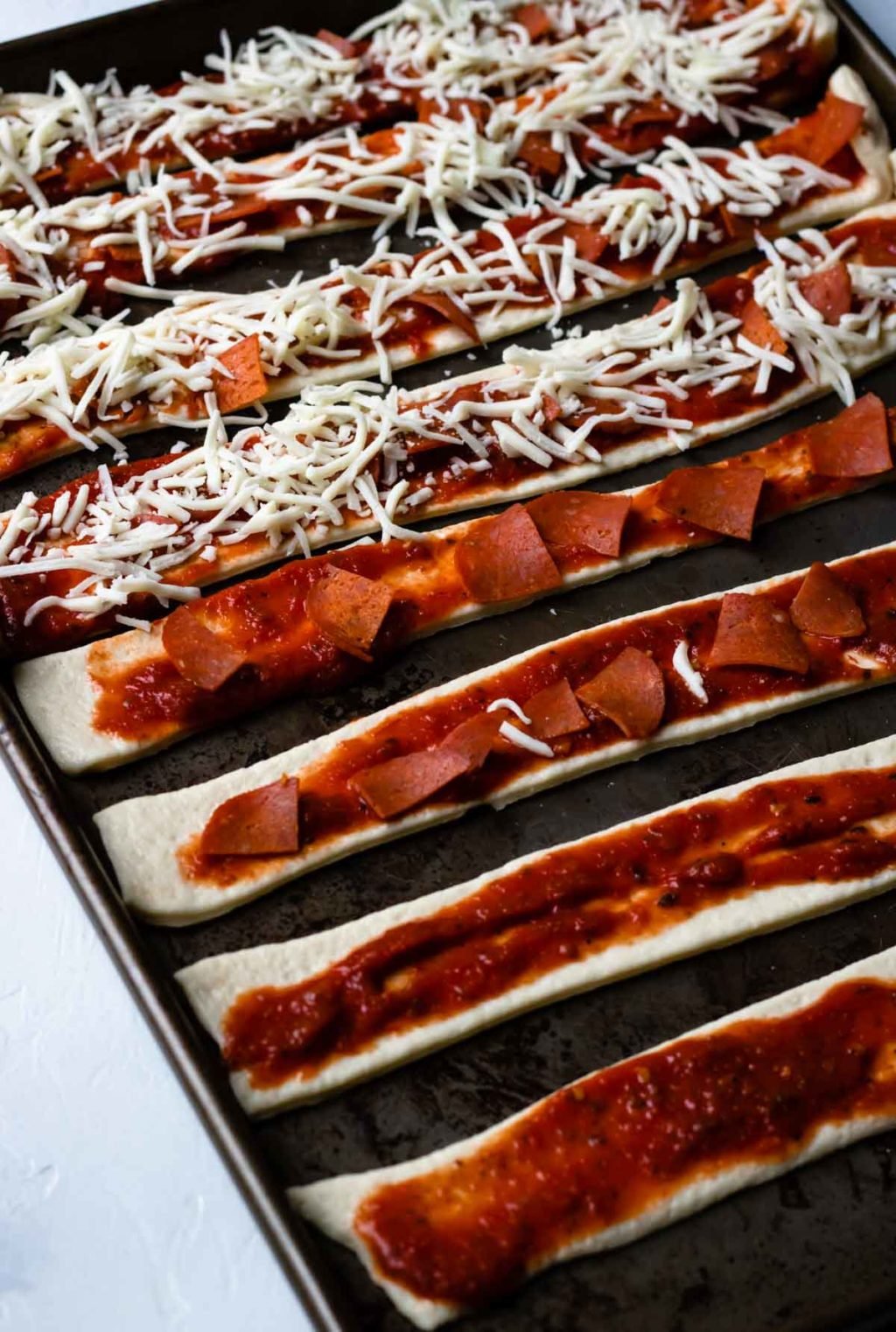 Pizza Roll Ups on a sheet pan topped with sauce, pepperoni, and cheese