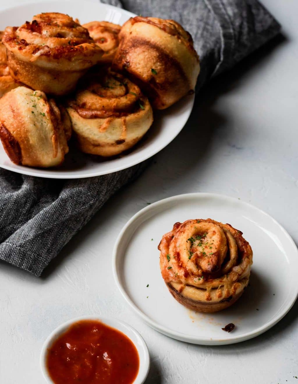 pizza roll ups in a white bowl, one roll up on a plate with marinara dipping sauce