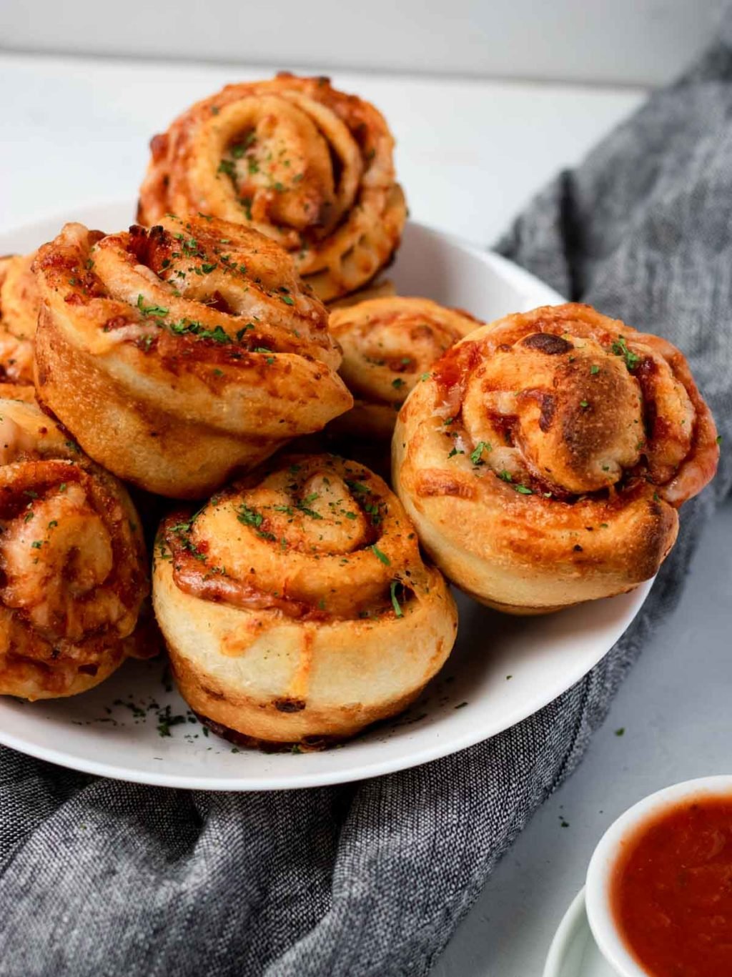 pizza roll ups in a white bowl with marinara on the side