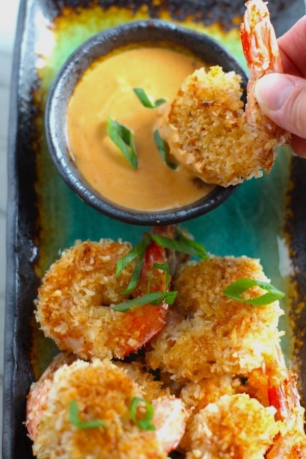 Coconut Shrimp being dipped into sriracha mayo