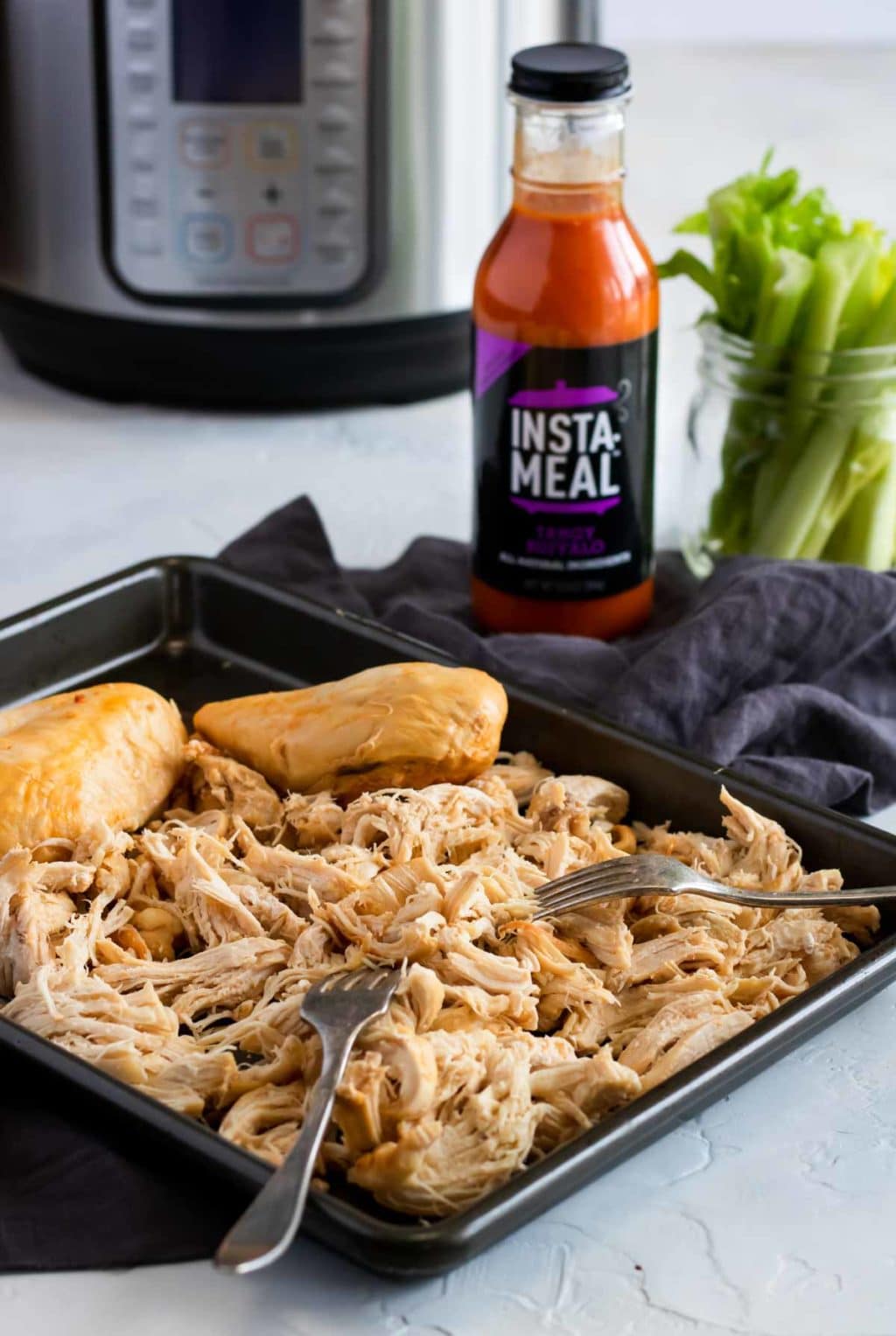 chicken shredded in a sheet pan with buffalo sauce in a bottle and the instant pot