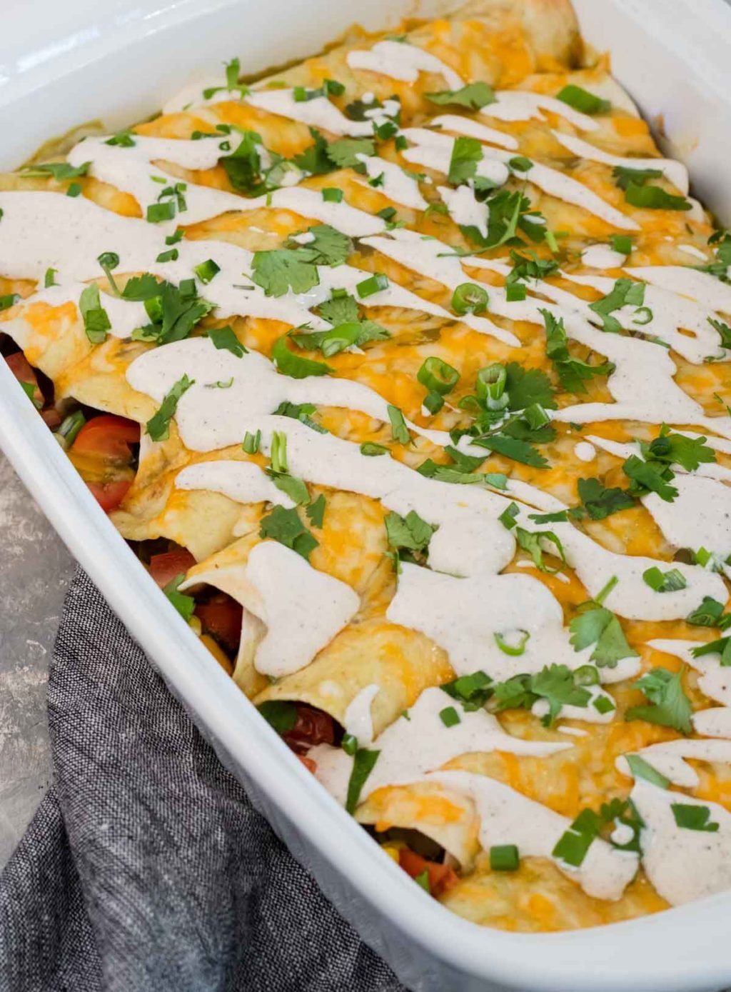 Veggie Enchiladas topped with Chili Lime Crema in a white glass baking dish