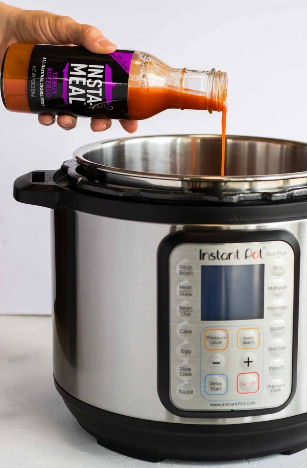 Pouring Tangy buffalo sauce into the instant pot