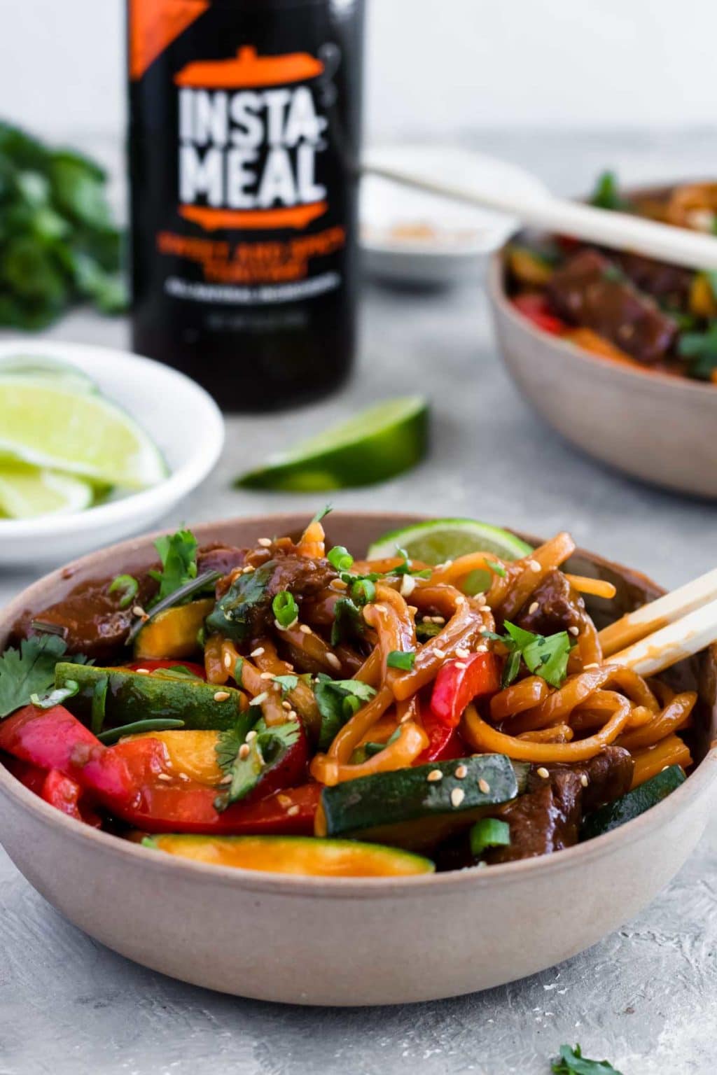 Instant Pot Teriyaki Beef Noodles in a bowl with an Instant Pot Sauce bottle in the background and a bowl of limes