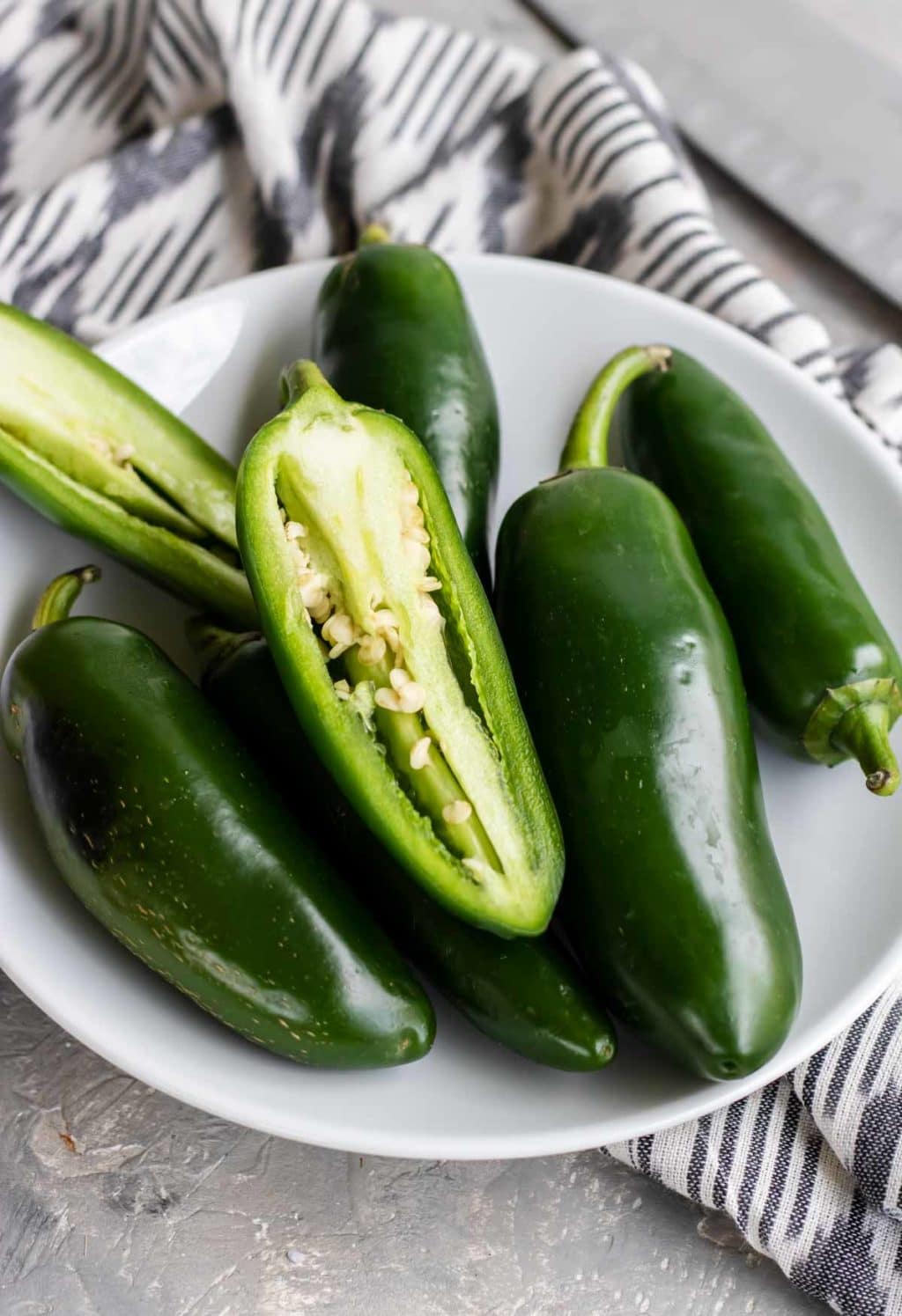 a white bowl of jalapenos with one split in half lengthwise